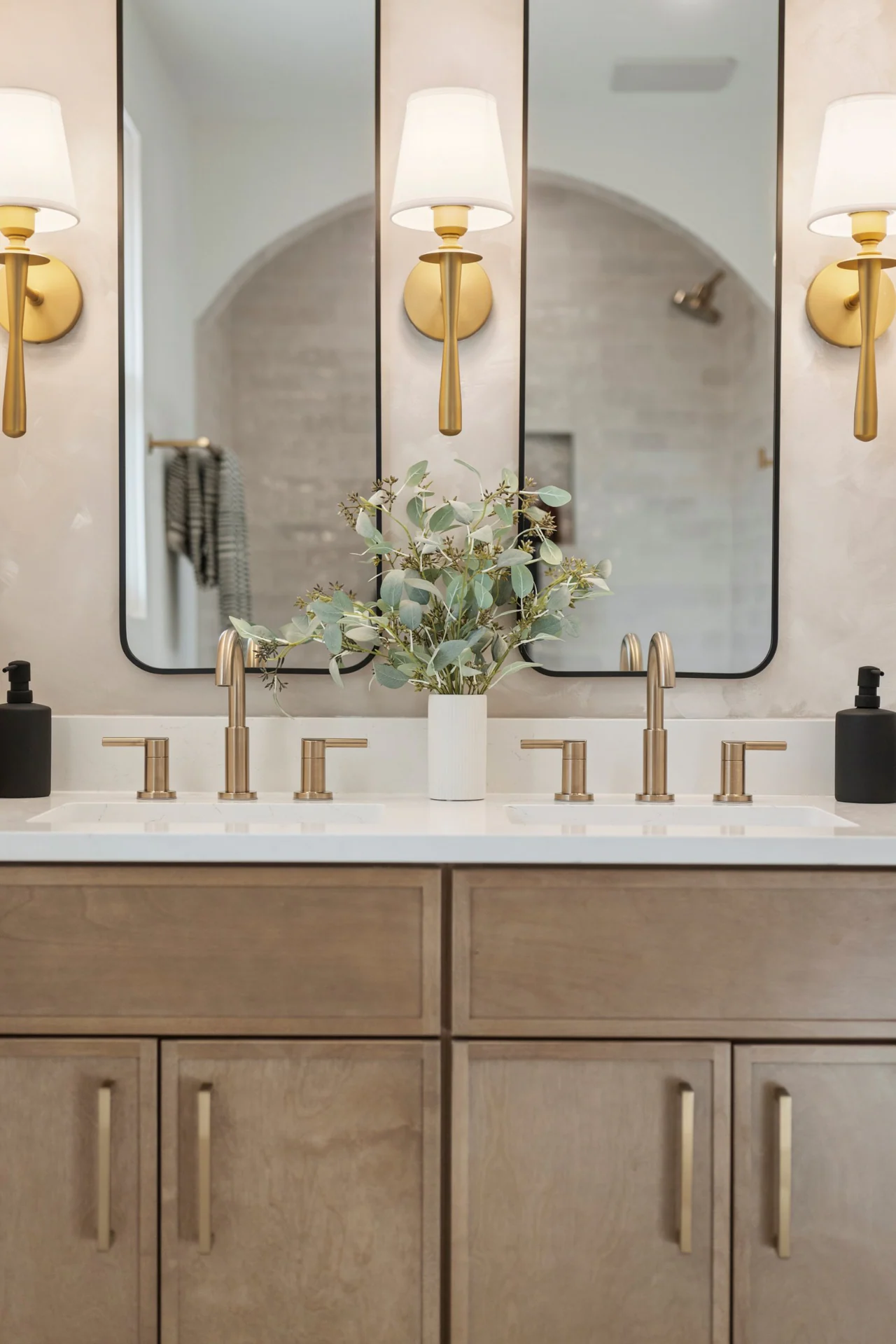 Double vanity with brass faucets, sconces and tall mirrors